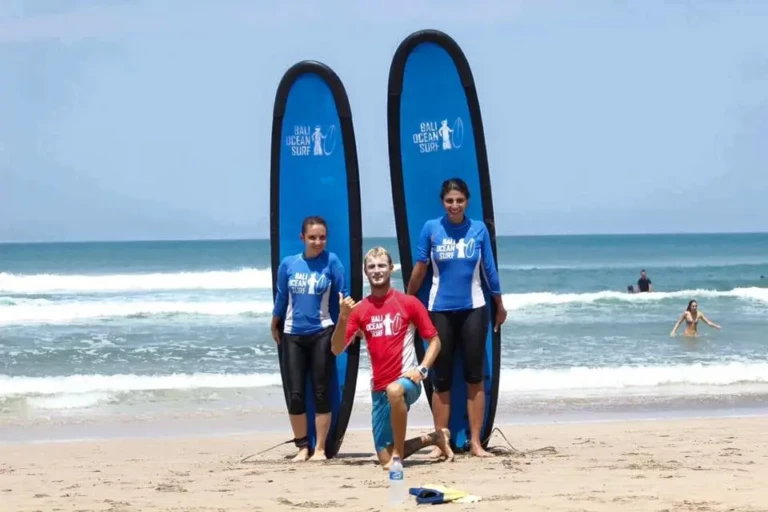 Moniteur de surf prenant la pose avec deux élèves devant leur planche