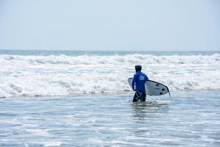 Elève dans l'eau avec sa planche de surf sous le bras