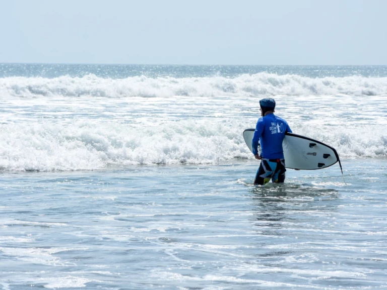Elève dans l'eau avec sa planche de surf sous le bras