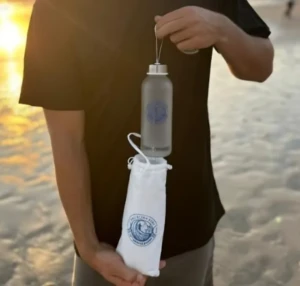 Man holding a Bali Ocean Surf thermos with its white logo pouch at sunset on Bali beach